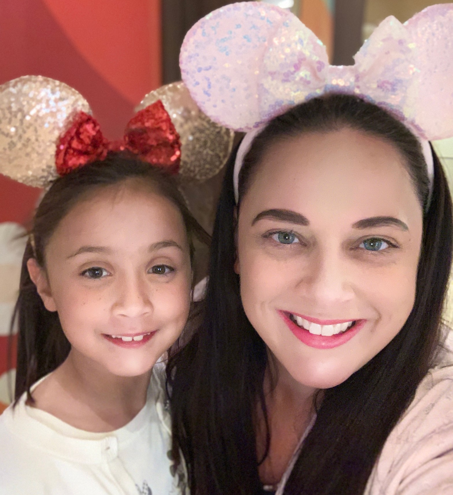 Jemma in gold, sequined Mouse ears with a red bow, Jen in pink sequined mouse ears with a pink bow, at Chef Mickey's at Walt Disney World